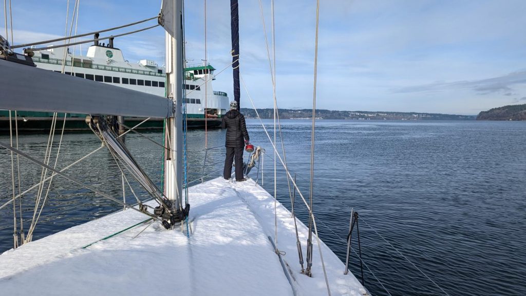 Friend up on the bow of the boat with snowy decks as we leave Tacoma, with a Washington State Ferry off the port bow